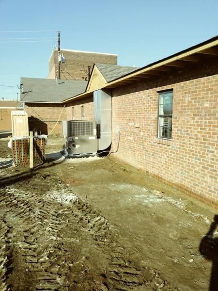 An exterior view of a brick building with a metal HVAC unit installed against the wall above a dirt construction site.