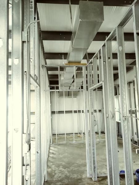 Interior view of a construction site showing metal wall studs, concrete flooring, and an overhead HVAC duct system.