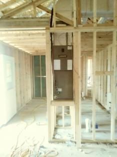 A brown HVAC furnace unit installed within an unfinished wooden wall frame in a room under construction.