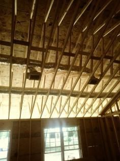 Wooden roof trusses and structural framing inside a house under construction, with visible ductwork and a window below.