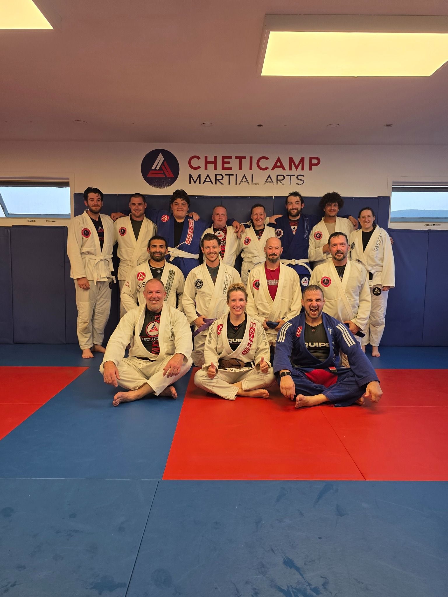 Jiu-jitsu team posing in white gis and blue uniform on mats inside a Cheticamp Martial Arts gym
