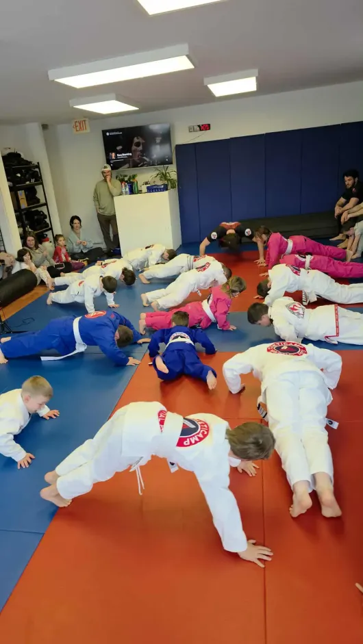 Children doing push-ups on mats in a martial arts studio with blue walls and red flooring