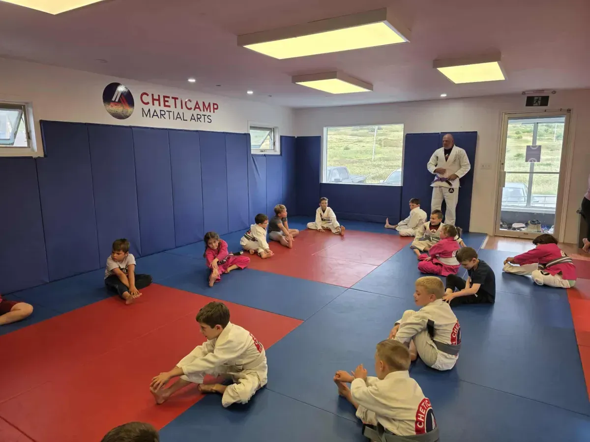 Children sitting on mats in a martial arts studio in Cheticamp, with an instructor standing at the front.