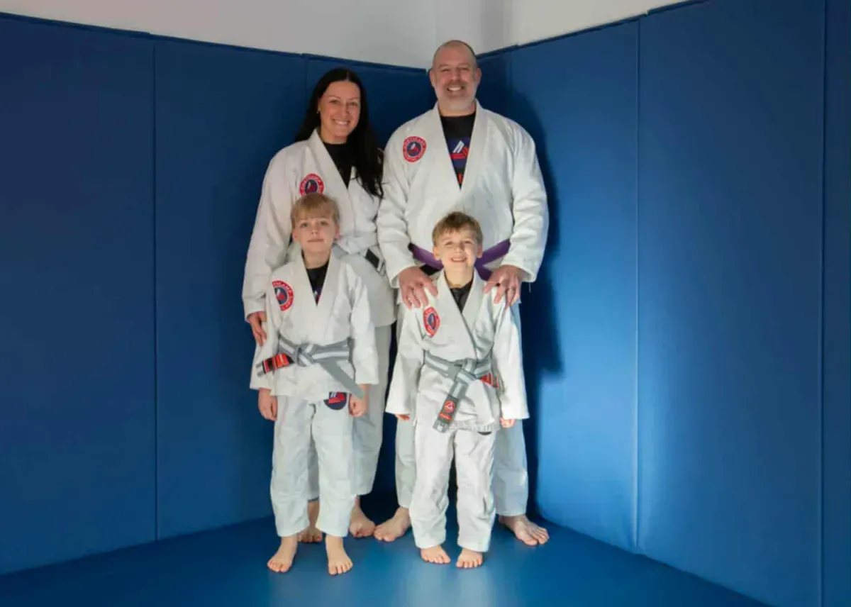 Four people in white martial arts gis posing on blue mats in a dojo in Cheticamp