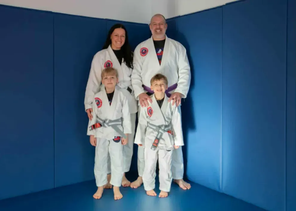 Four people in white martial arts gis posing on blue mats in a dojo