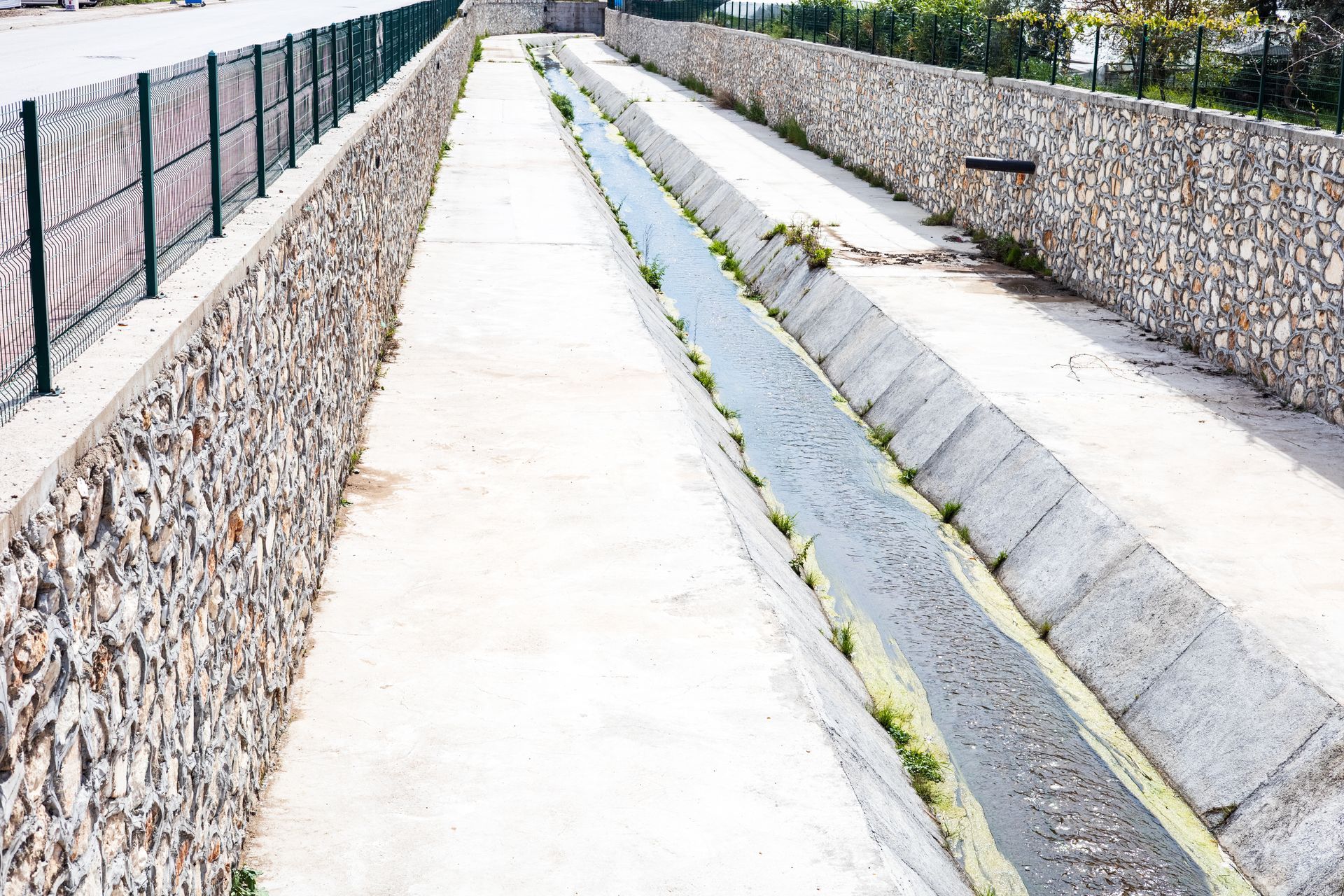 A small stream trickles through a gap in a retaining concrete wall A small stream trickles through a gap in a retaining concrete wall