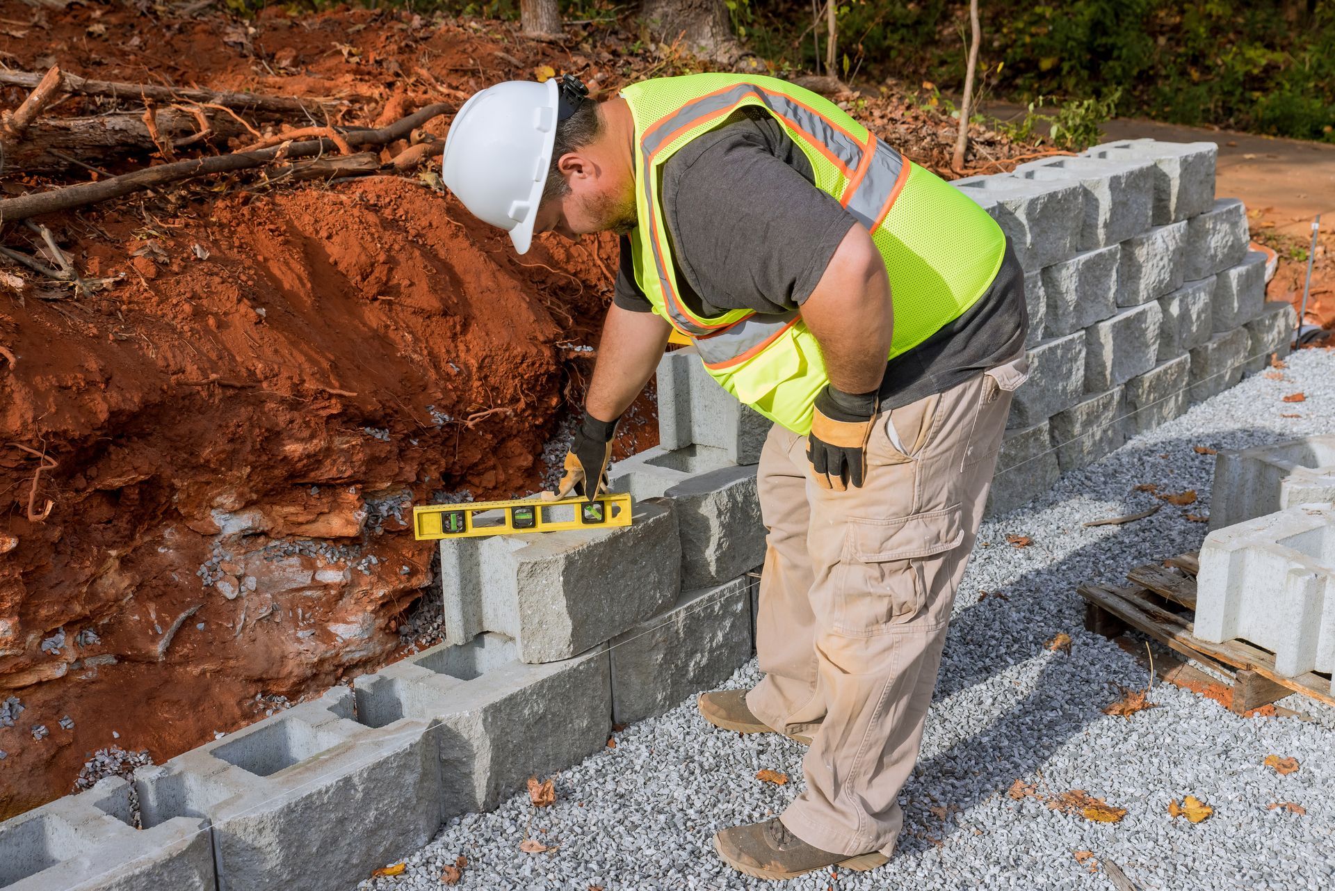 A contractor during the retaining wall installation of a new large block at a construction site. A contractor during the retaining wall installation of a new large block at a construction site.