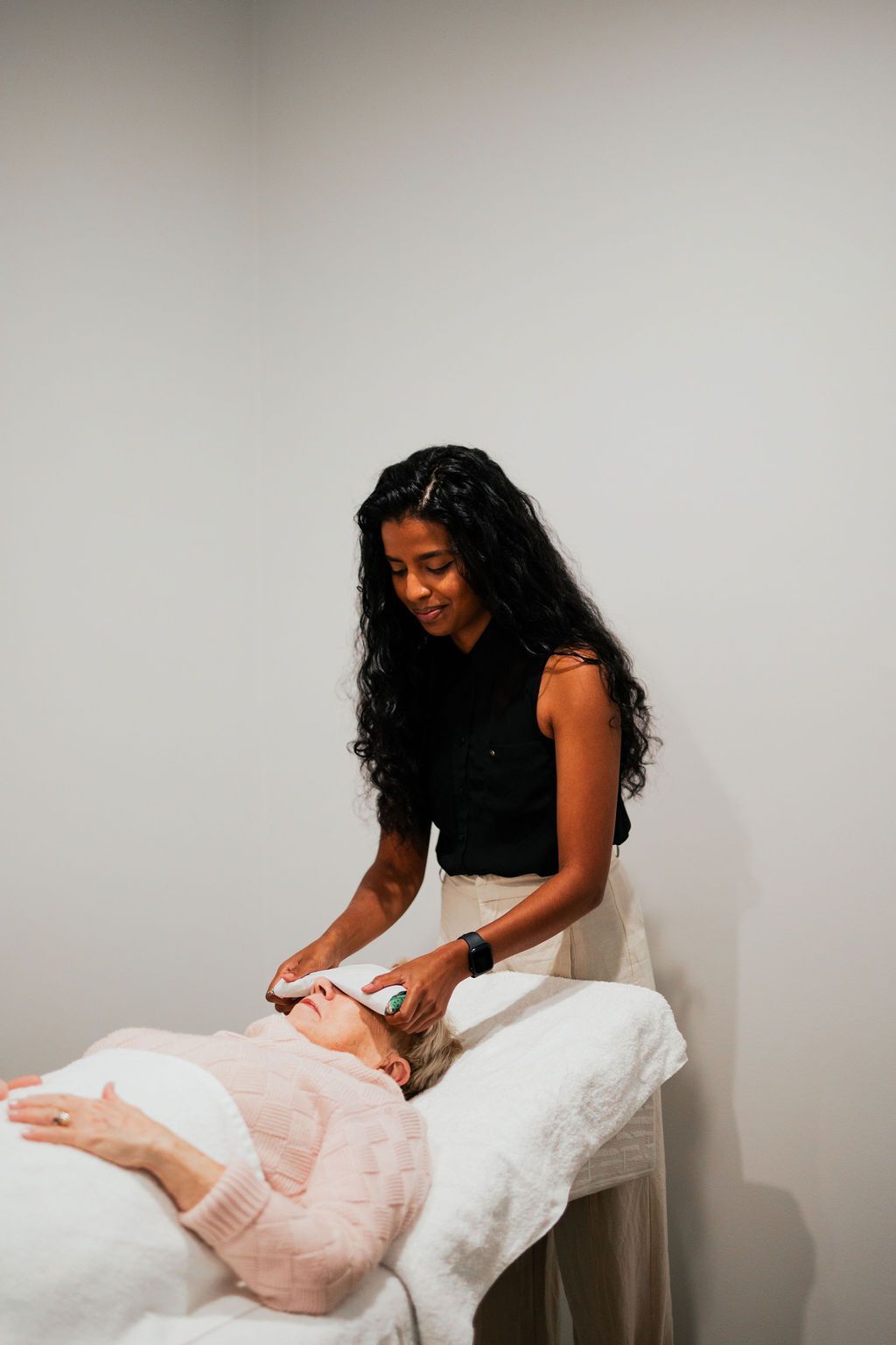 Massage therapist working on a client lying face down on a treatment table in a plain room