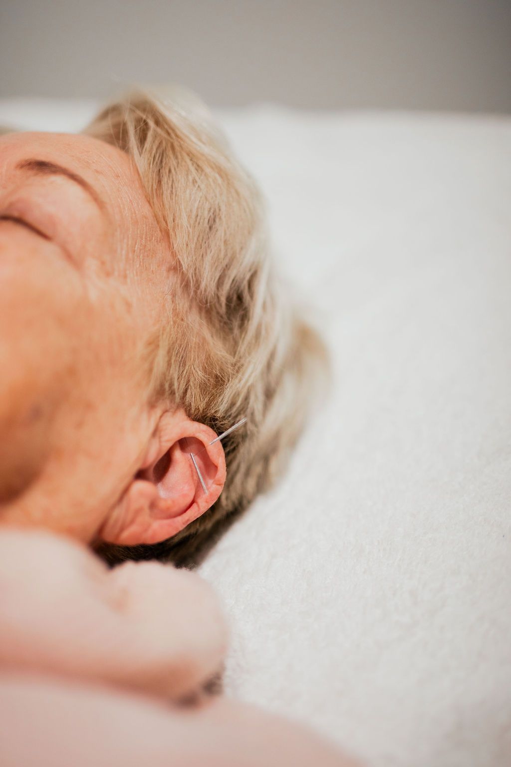 Close-up of a person resting on a white pillow, showing part of the face and ear in soft light