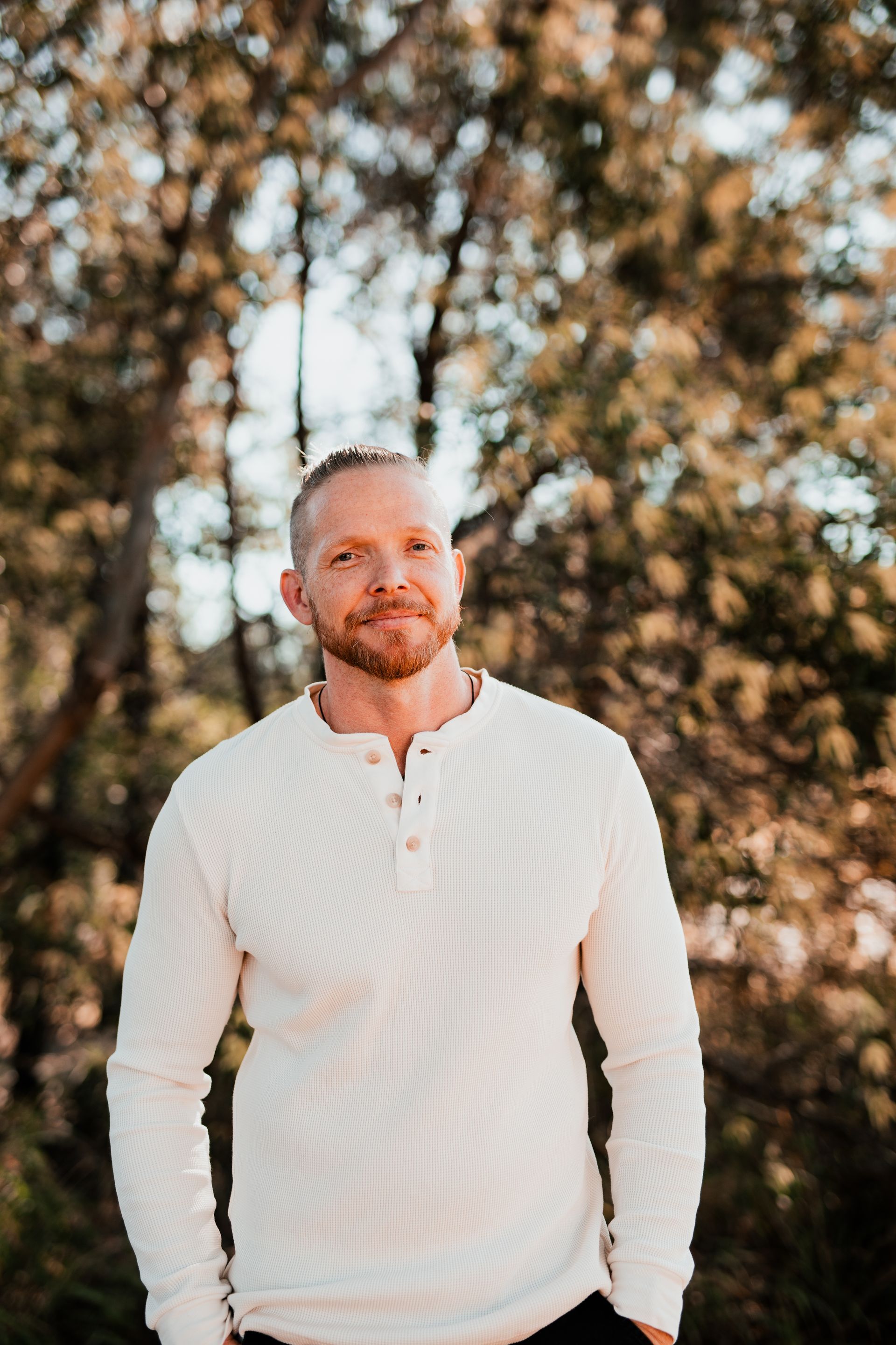 Man in a white shirt standing outdoors with blurred trees in the background