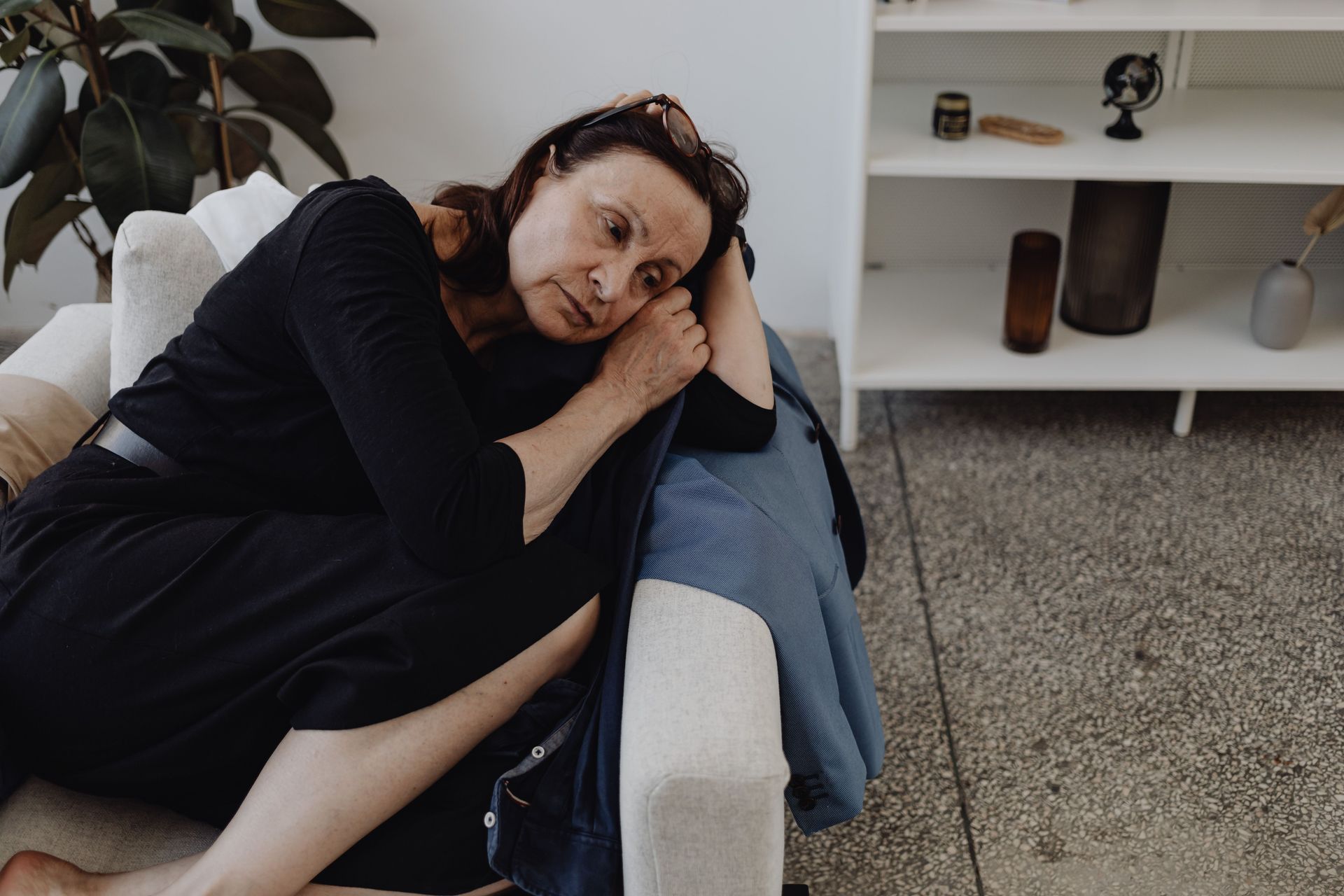Person in dark clothing leaning on a couch, resting their head on a pillow in a modern living room.