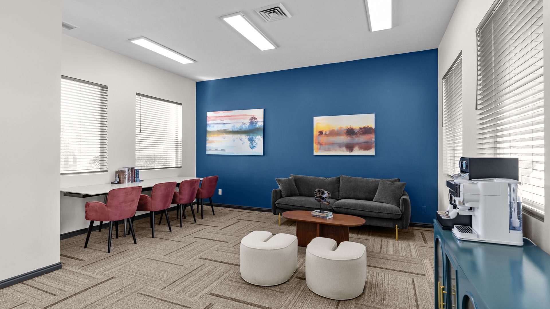 Modern waiting room with blue accent wall, pink chairs, couch, coffee table, and two white ottomans