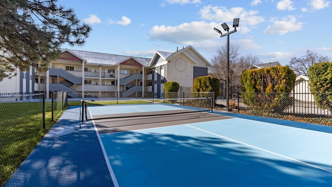 Outdoor blue tennis court in front of a light-colored apartment building on a sunny day