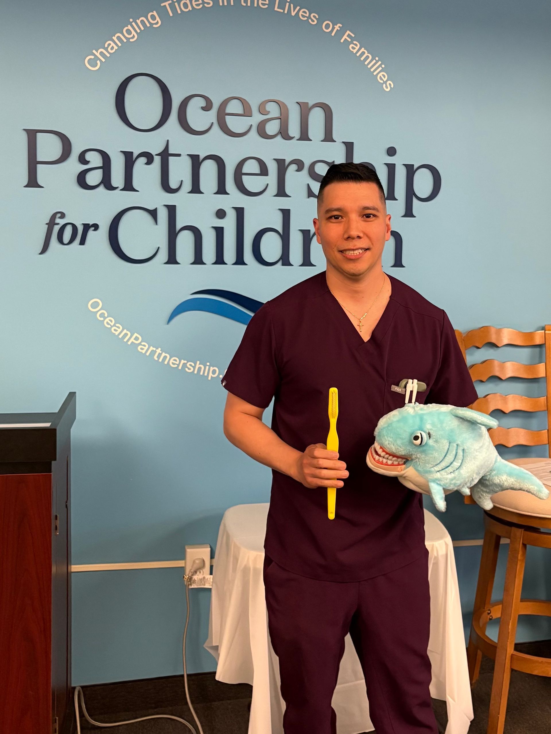 Man in purple scrubs holding toothbrush and stuffed whale in front of