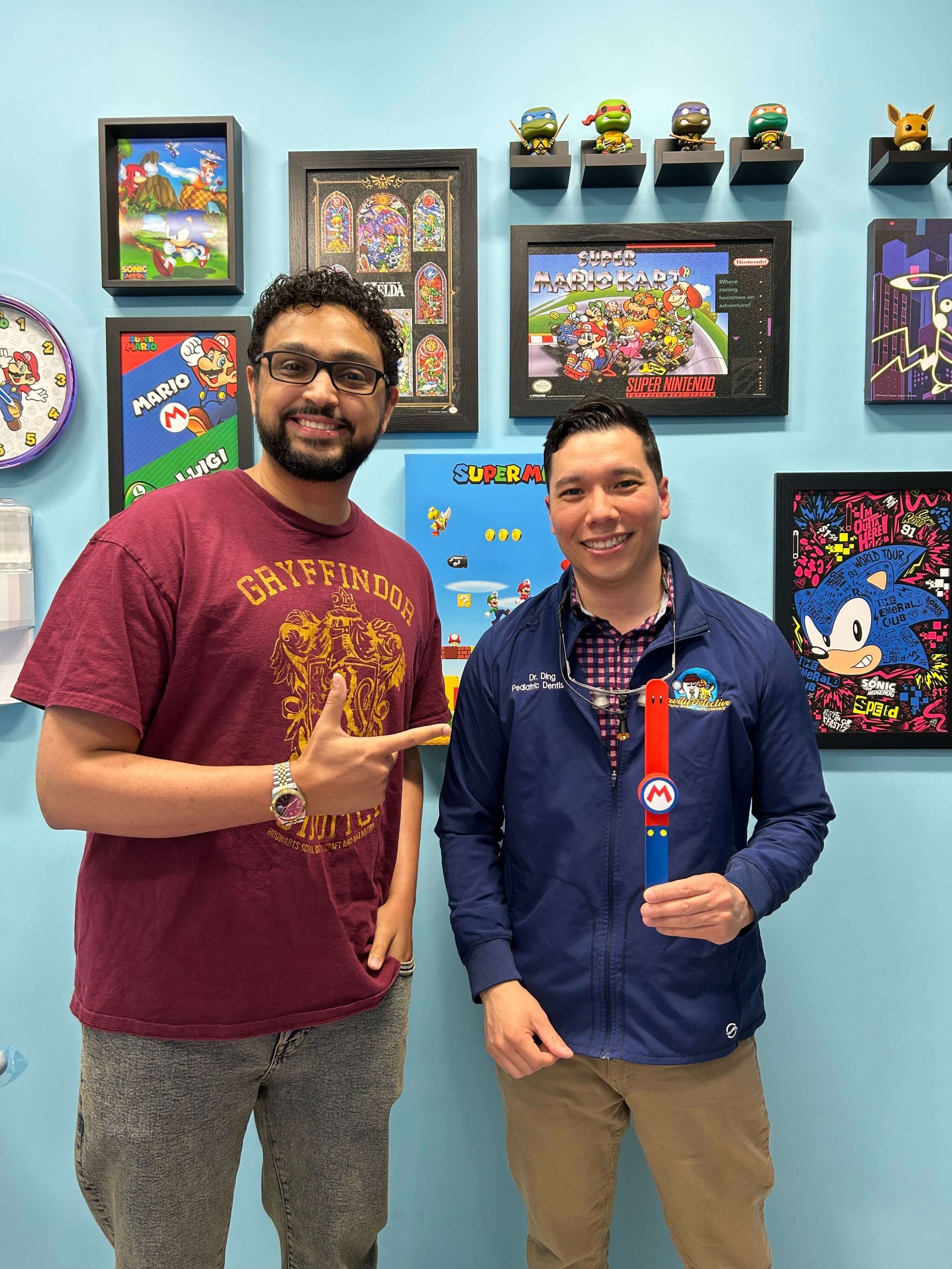 Two men posing in a colorful art display room, one pointing at the other and smiling.