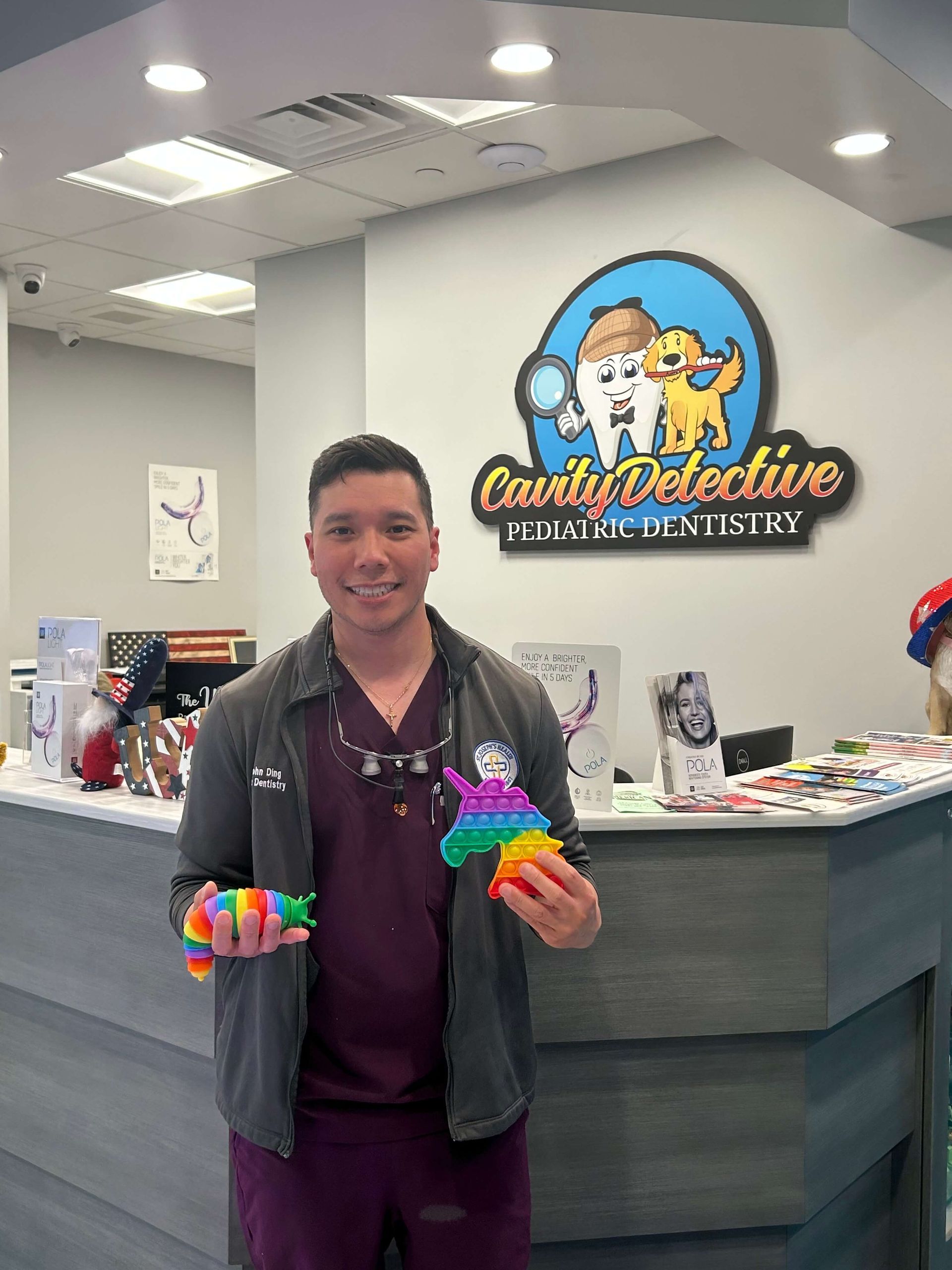 Dentist holding colorful toys, smiling at the camera, inside a pediatric dentistry office.