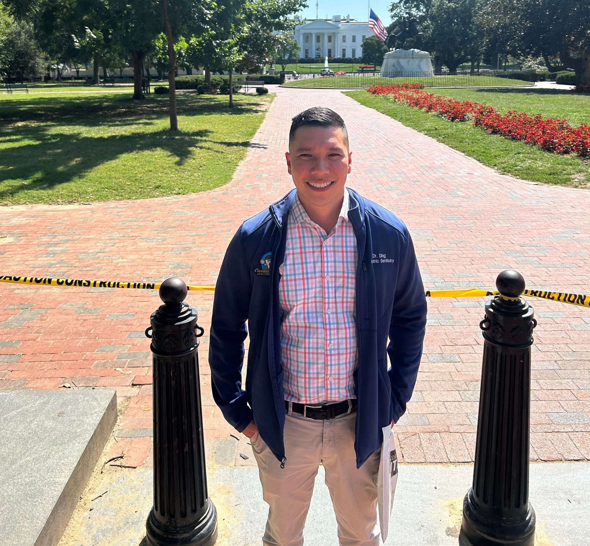 Man in a blue jacket and khakis smiles in front of the White House on a sunny day.