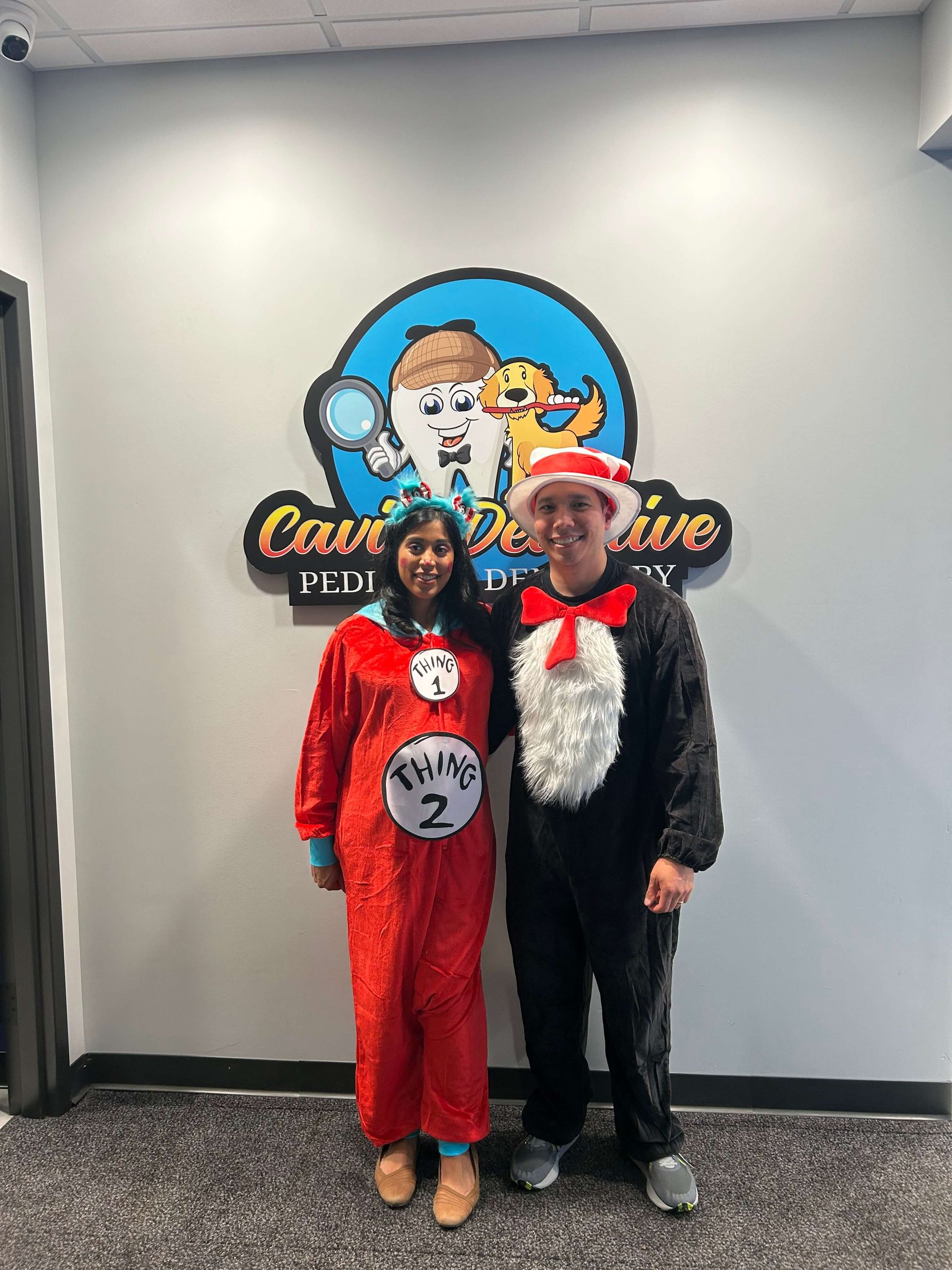 Two people in costumes posing in front of a Cat in the Hat mural.