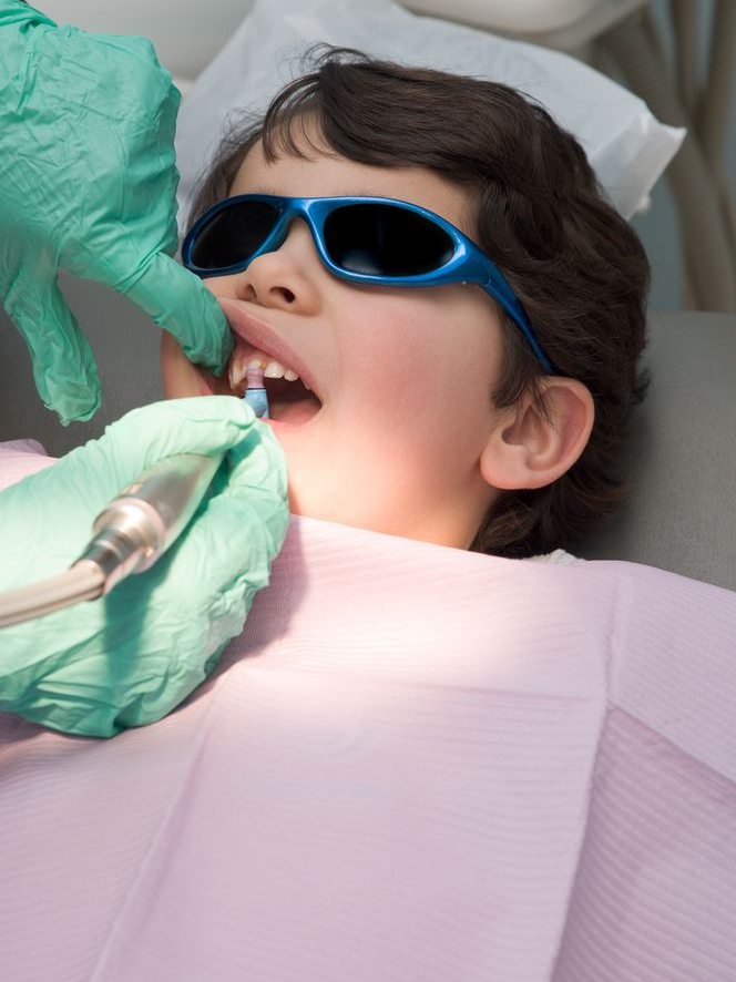 Dentist examining a smiling patient under a bright dental lamp in a clinic