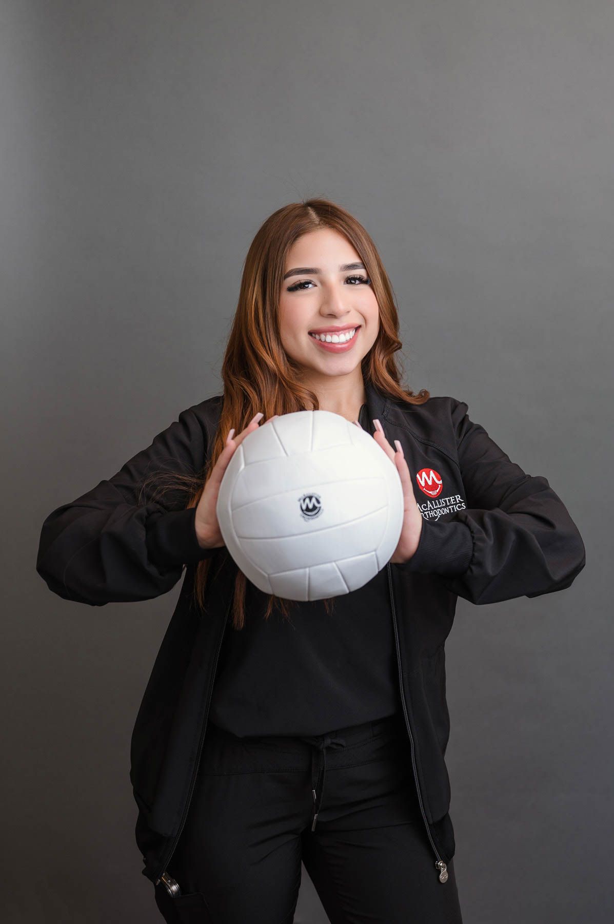 A woman in a black jacket is holding a volleyball in her hands.