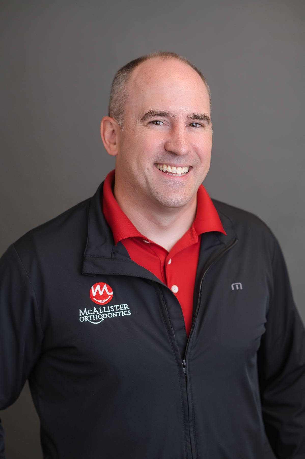 A man wearing a black jacket and a red shirt is smiling for the camera.