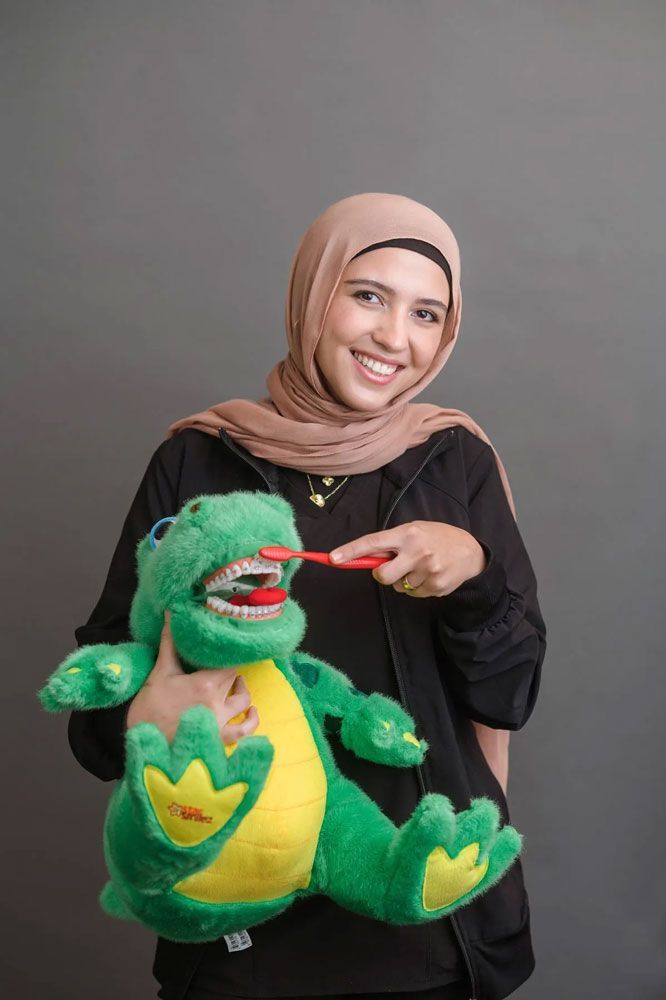 A woman in a hijab is brushing her teeth with a toy dinosaur.