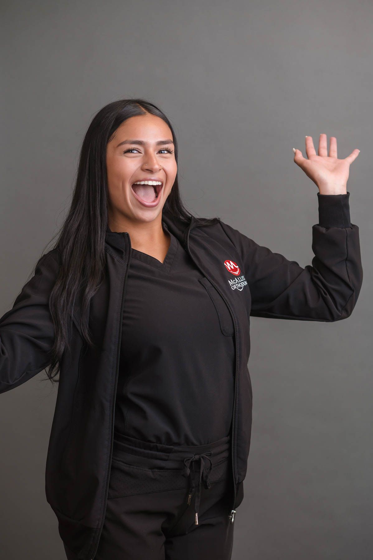 A woman in a black jacket and black scrubs is waving her hand.