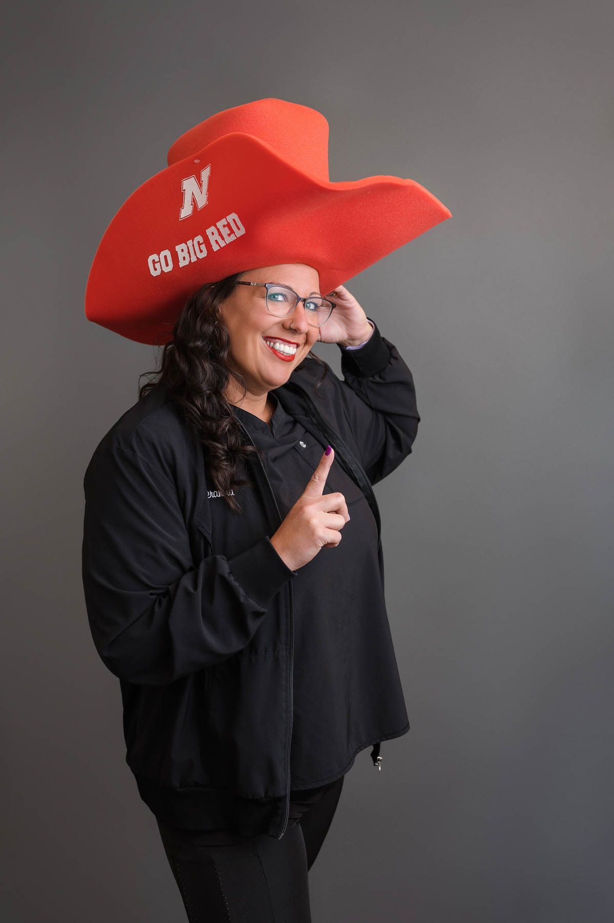 A woman is wearing a red cowboy hat and giving a thumbs up.