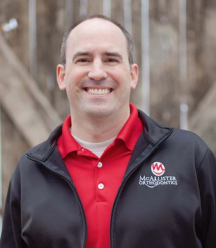A man wearing a red shirt and a black jacket is smiling.