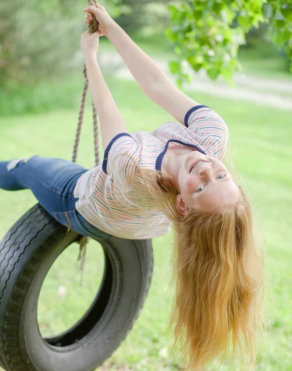 A woman is upside down on a tire swing.