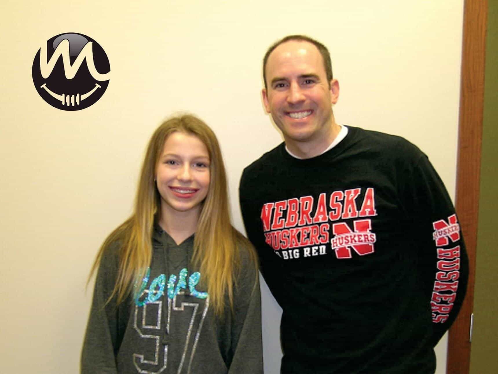 A man and a girl are posing for a picture and the girl is wearing a nebraska shirt