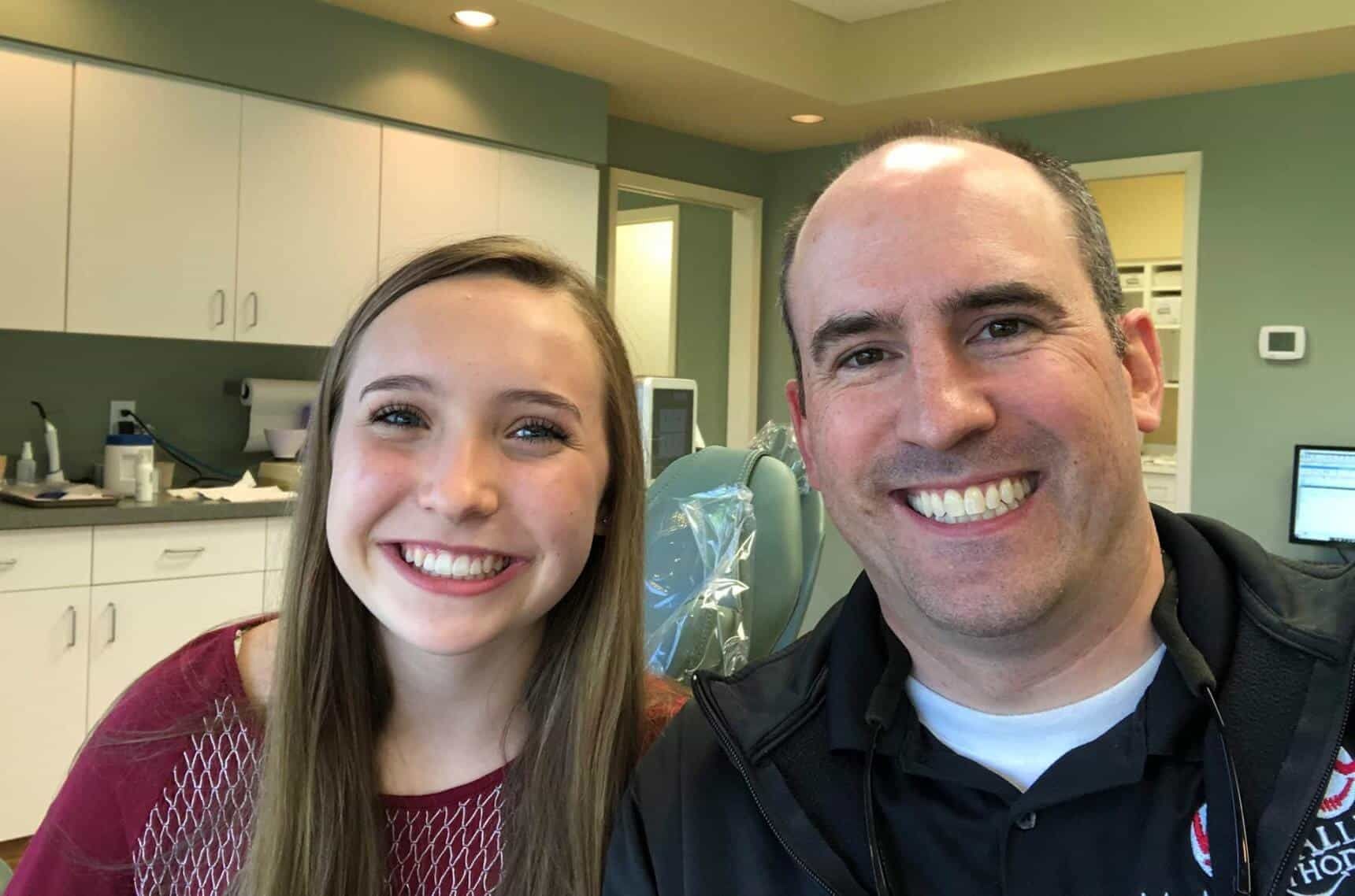 A man and a girl are smiling for the camera in a dental office.