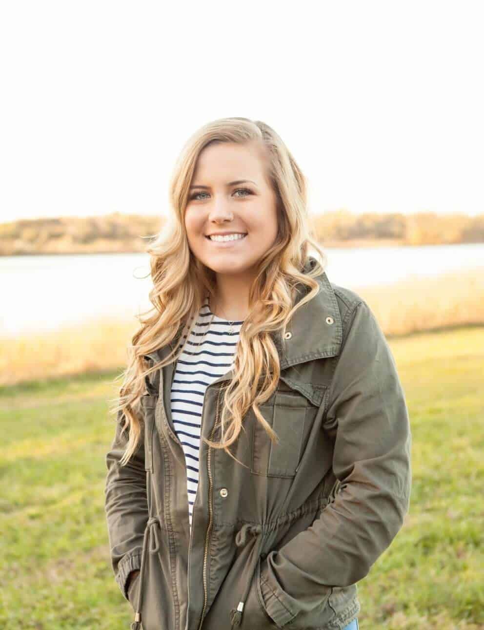 A woman in a green jacket and striped shirt is standing in a field.