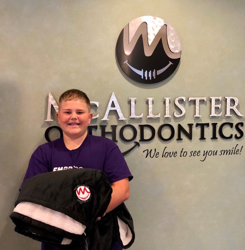 A young boy stands in front of a wall that says McAllister Orthodontics.