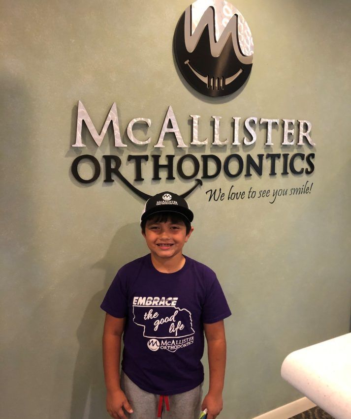 A young boy is standing in front of a McAllister Orthodontics sign.