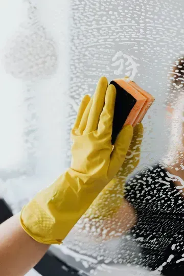 Yellow-gloved hand wiping a fogged glass pane with a sponge