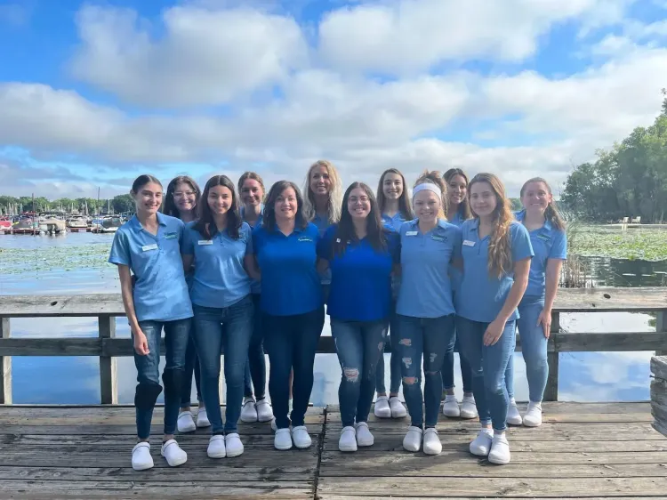 Group of people in blue shirts standing on a dock by the water under a partly cloudy sky