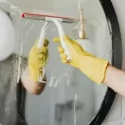 service Yellow-gloved hands cleaning a circular mirror with a white spray bottle and cloth