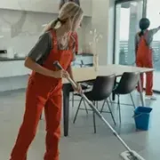 service Woman mopping a bright kitchen with orange overalls while another cleans near the window