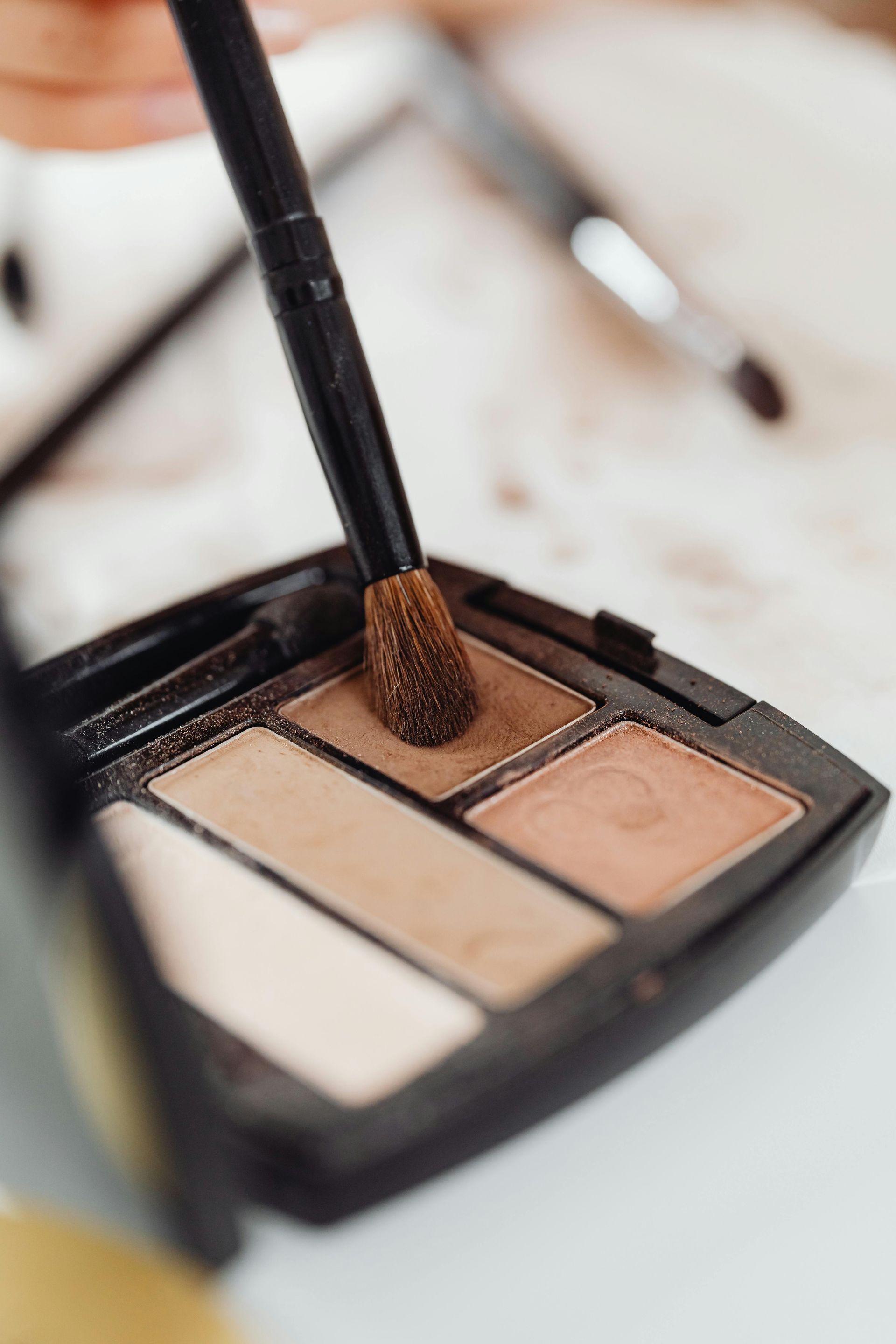Makeup Brush Picking Up Eyeshadow From A Palette With Four Neutral Shades — Penelope's Beauty in Newcastle, NSW