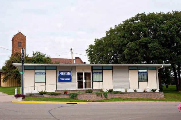 Small white building with blue awning and sign, seen from the street with trees and a brick tower behind it