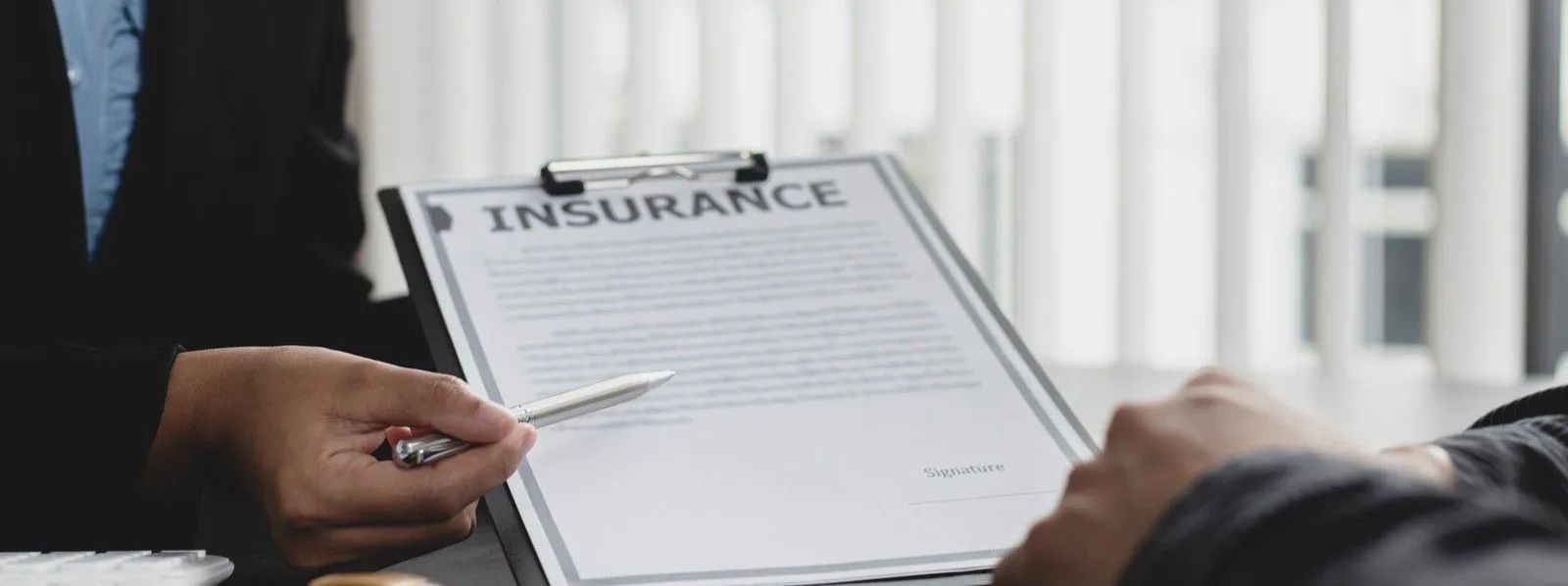 Hands holding an insurance document on a desk in an office setting