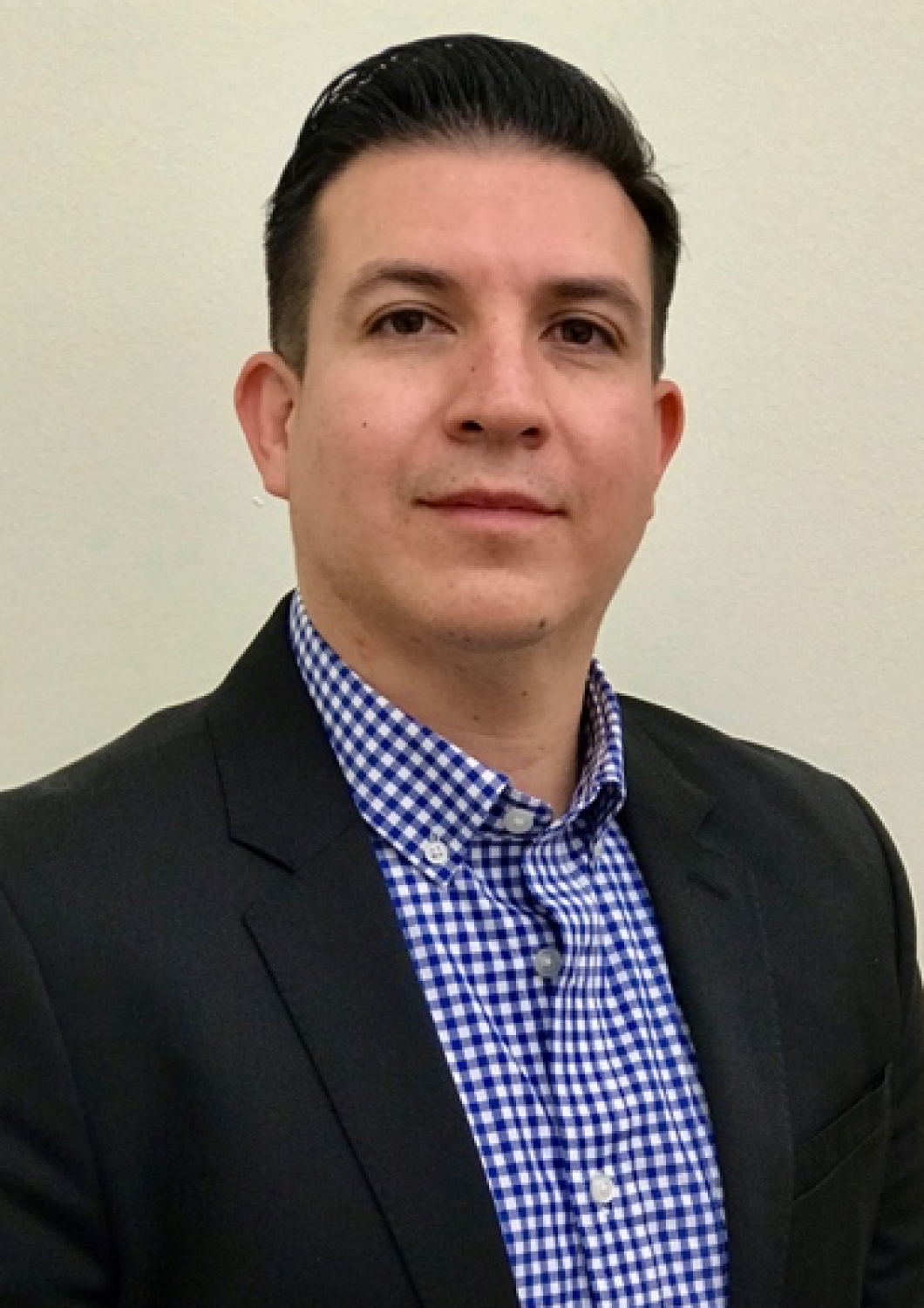 Portrait of a man in a black blazer and blue checkered shirt against a plain light background