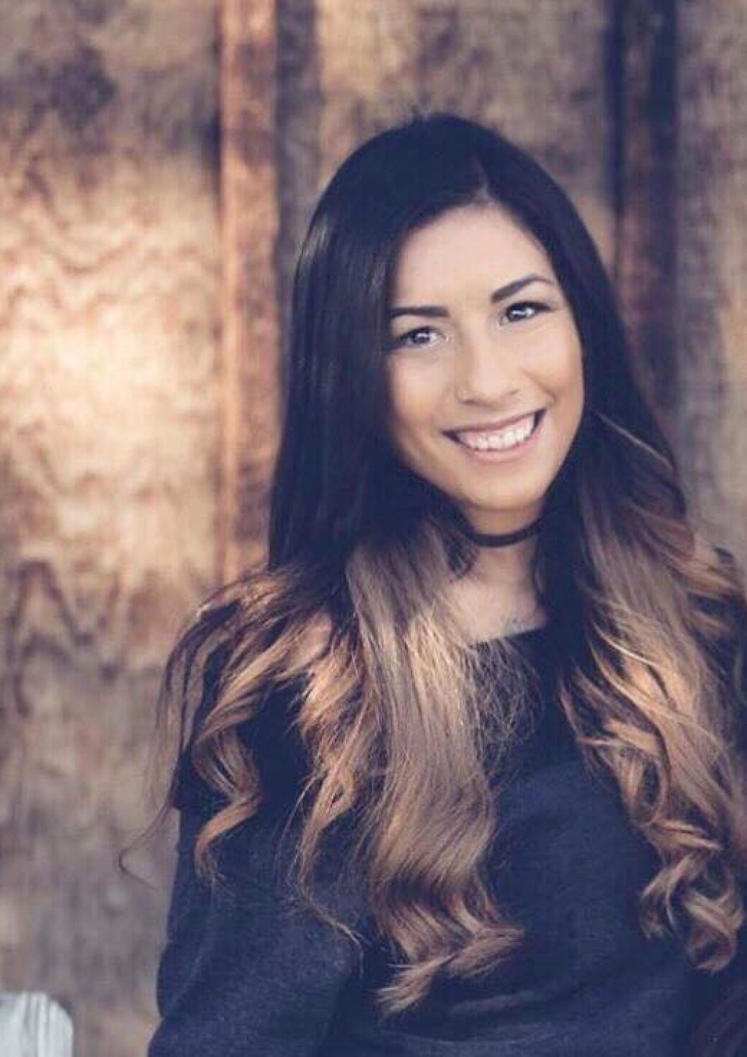 Smiling woman with long wavy hair in a dark top against a rustic wooden background