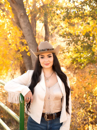 Woman in a tan hat and vest leaning on a railing in a sunlit autumn park