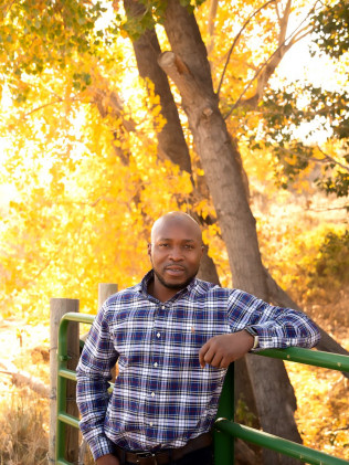 Man leaning on a green railing outdoors среди autumn trees in a blue plaid shirt