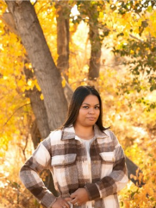 Person in a plaid shirt standing outdoors among autumn trees, with warm golden leaves in the background.