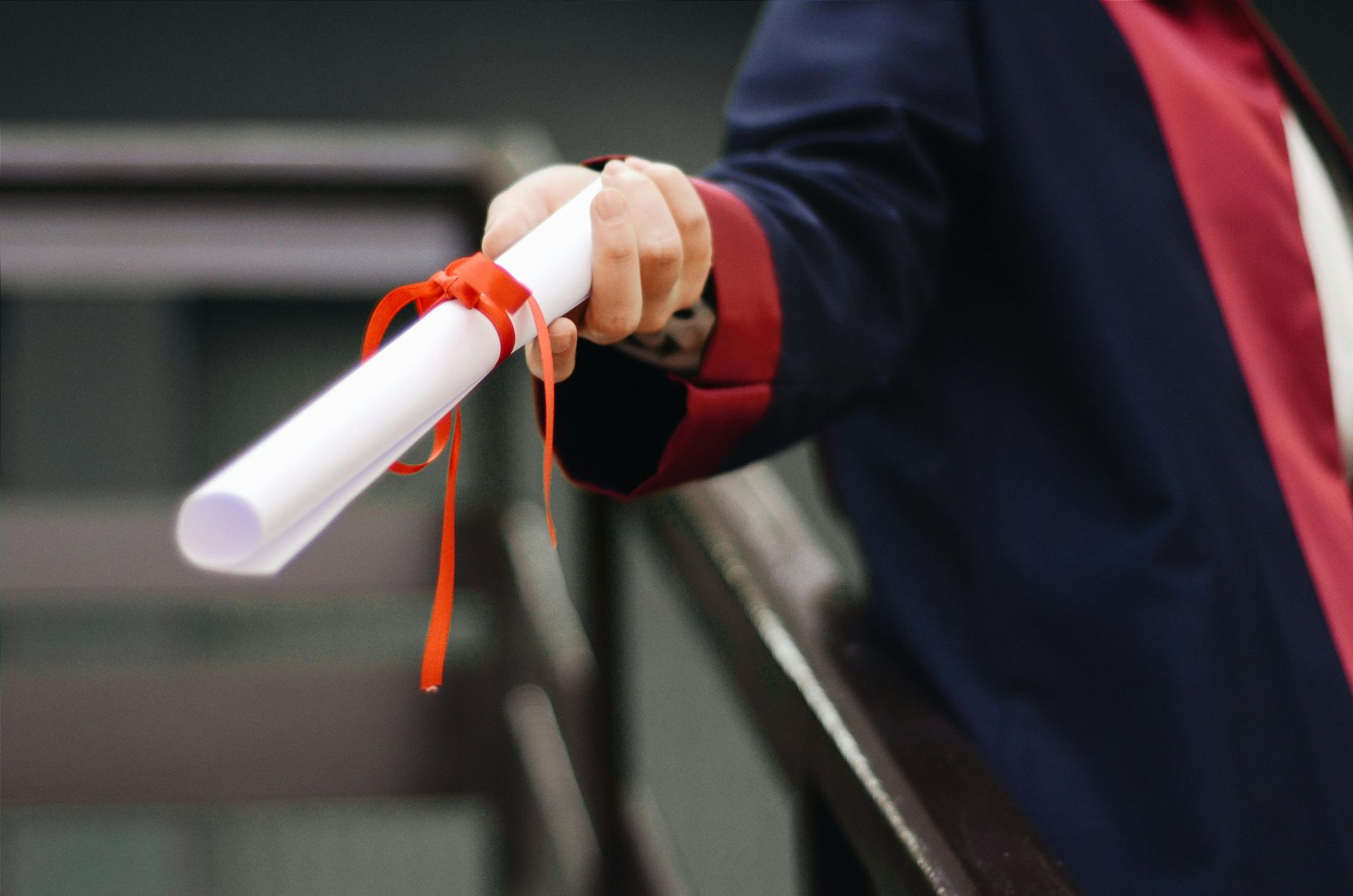 Hand holding a rolled diploma tied with orange ribbon at a graduation ceremony