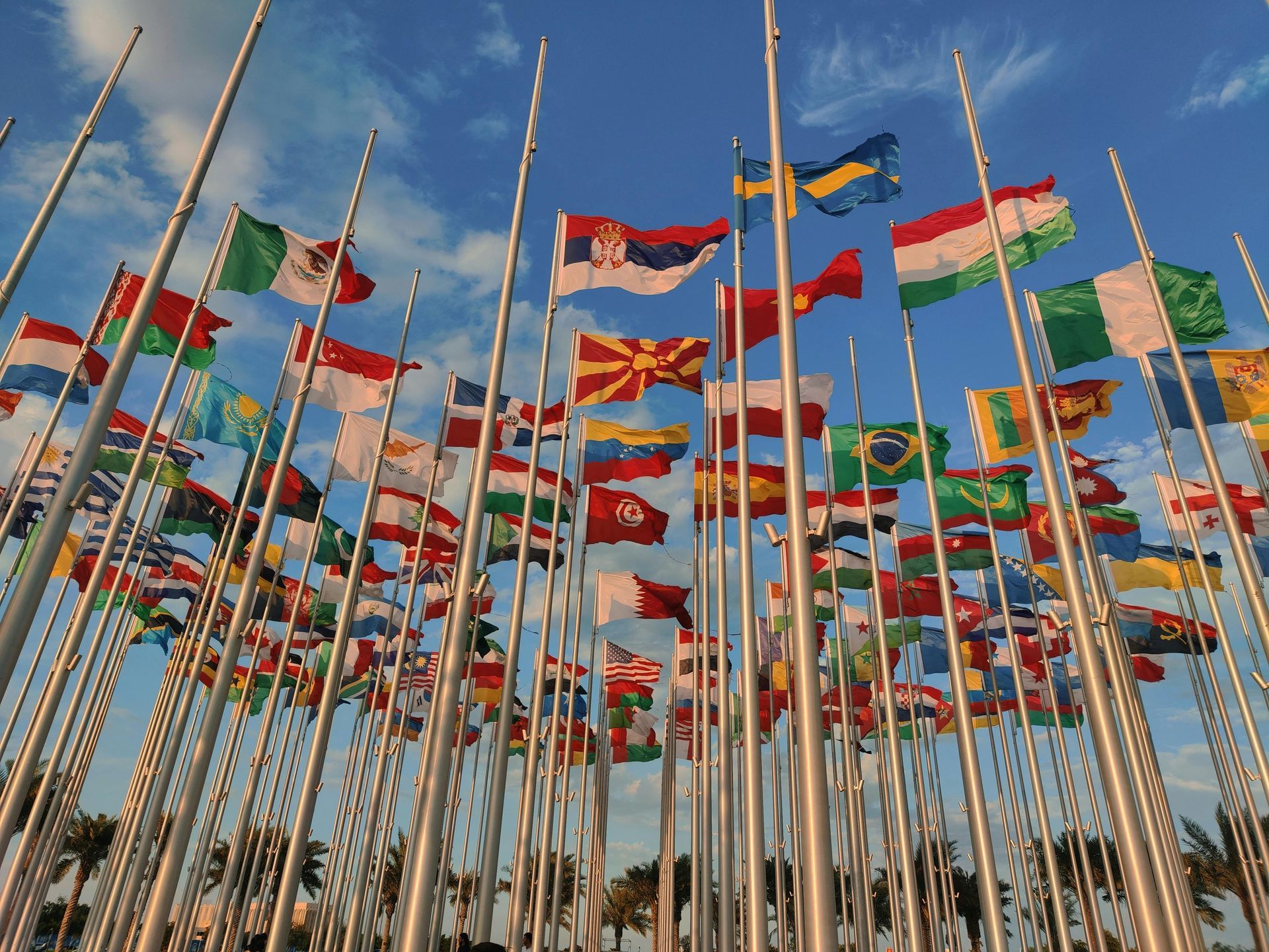 Many colorful national flags on tall poles waving against a blue sky