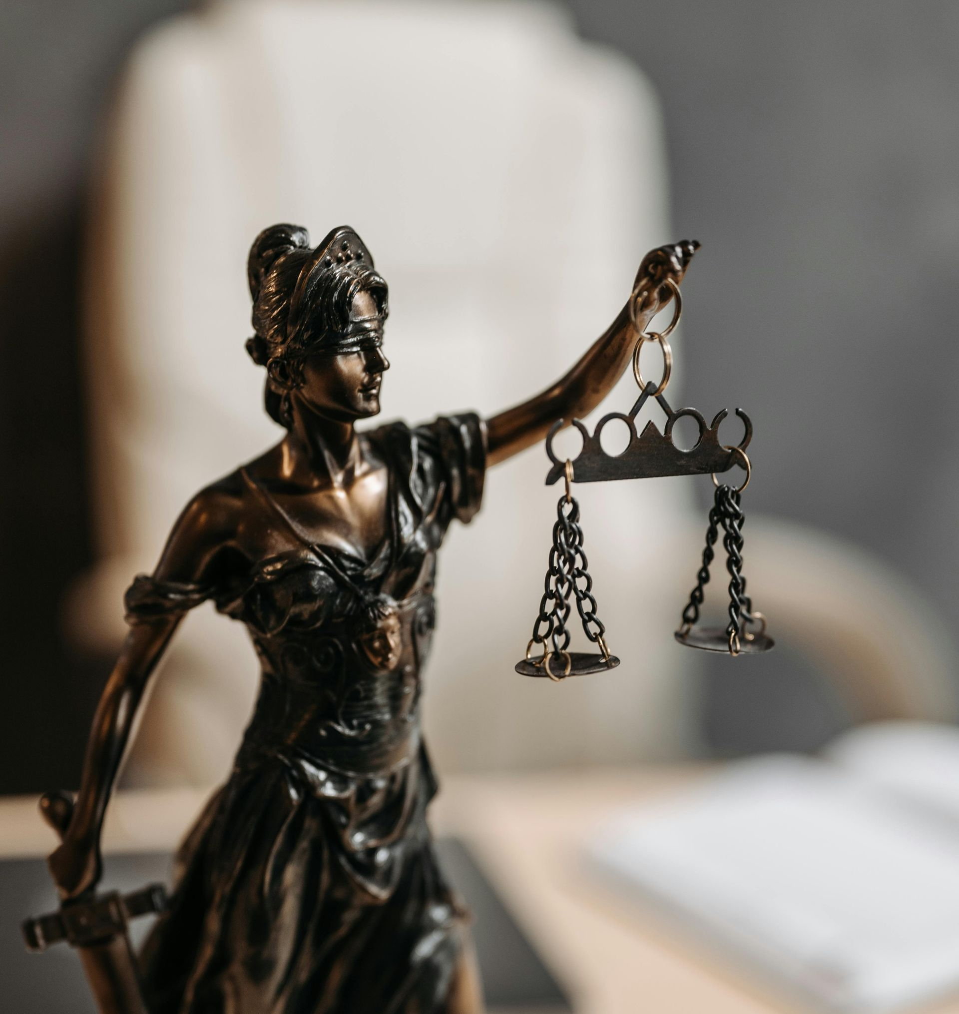 Bronze Lady Justice statue holding scales, with a blurred gavel in the background